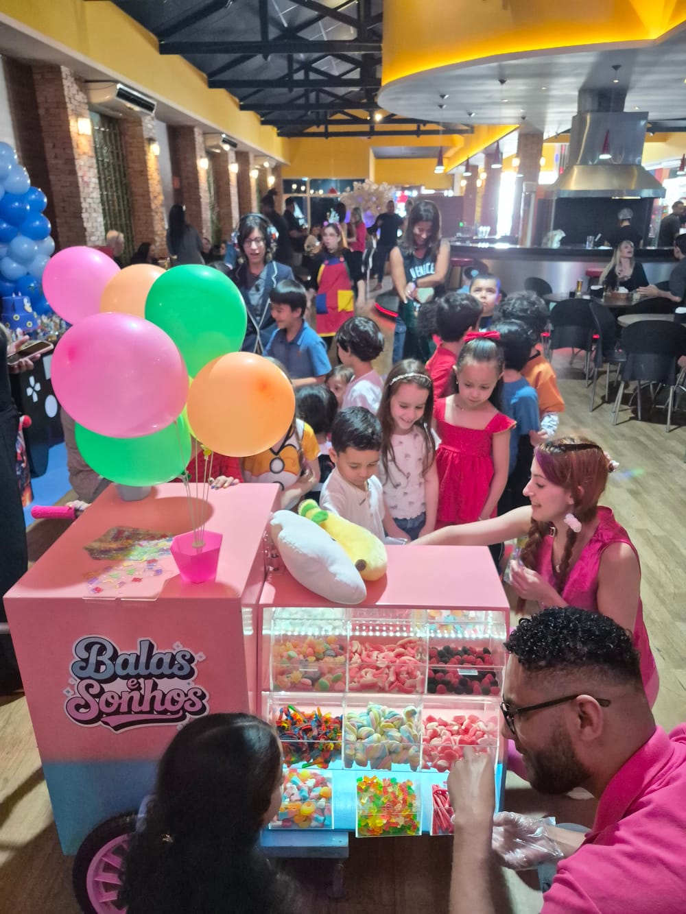 Equipe da Balas e Sonhos servindo doces a um grupo de crianças em volta do carrinho rosa com balões