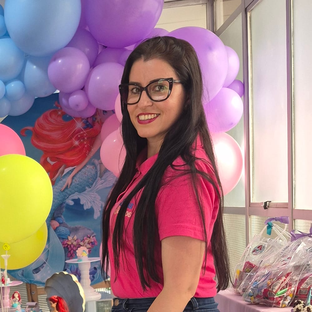 Priscilla, fundadora da Balas e Sonhos, sorrindo de camisa rosa da marca em uma festa